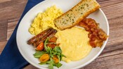 Un plato de huevos revueltos, polenta cremosa de mascarpone, tocineta y salchichas de Primo Piatto