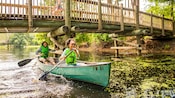 A mother and daughter paddling a canoe under a bridge at Disney’s Fort Wilderness Resort and Campground