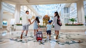 Family guests walking into the lobby of the Grand Floridian with luggage bags and mouse ears. 