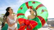 Two women smiling while holding onto an inflatable inner tube resembling a Christmas wreath