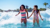 2 niñas de la mano mientras chapotean en la piscina de olas del parque acuático Disney’s Typhoon Lagoon