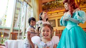 A child in a Cinderella dress and 2 other children smile as they meet Ariel