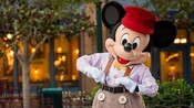 Mickey vestido con pantalones, una camisa abotonada, una corbata de moño, suspensores y una gorra.