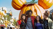 Two couples posing for a picture by the giant Mickey pumpkin on Main Street, USA, in Disneyland Park