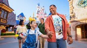 A young girl wearing a Minnie Mouse headband walking with her dad through Disneyland Park with Sleeping Beauty Castle in the background