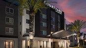 Landscaped with palm trees, the modern exterior of the Courtyard by Marriott Anaheim Resort.
