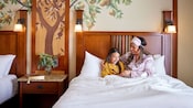 A mother and daughter enjoy time together, while sitting in bed, in their Disneyland Resort hotel room.