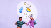 At Pixar Place Hotel, 2 kids skip together while one child holds a balloon and the other child holds a plush