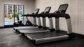 Three treadmills and a stationary bike in a gym with a window overlooking the pool at Courtyard by Marriott Anaheim Theme Park Entrance