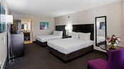 Two king beds with a table between them, a tall mirror on the wall, a bureau and a table and chair