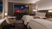 A hotel room at the Westin Anaheim Resort with a table, TV, 2 queen beds, 2 chairs and a balcony with a view of fireworks over Disney California Adventure Park