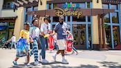A family holding shopping bags and Disney merchandise walks past the World of Disney store.