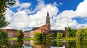 El campanario del ayuntamiento de Kiel con vistas a un lago rodeado de exuberantes árboles