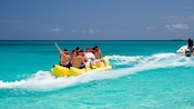 8 people riding on a banana boat pulled by a motorboat