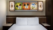 Standard Room with lit up artwork of animated Disney Characters, above a bed