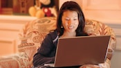A woman sits in an armchair looking at the screen of her laptop computer