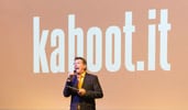 A man with a microphone speaking to an audience in front of a screen with the words kahoot it projected on it