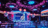 A modern event space with monitors, colorful lighting and cocktail and standard tables A modern event space with monitors, colorful lighting and cocktail and standard tables