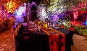 In a small courtyard surrounded by foliage, an elegant dining table with candles and a colorful table runner
