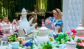 Alice from Alice in Wonderland sitting at a dining table decorated in a Mad Hatter Tea Party theme
