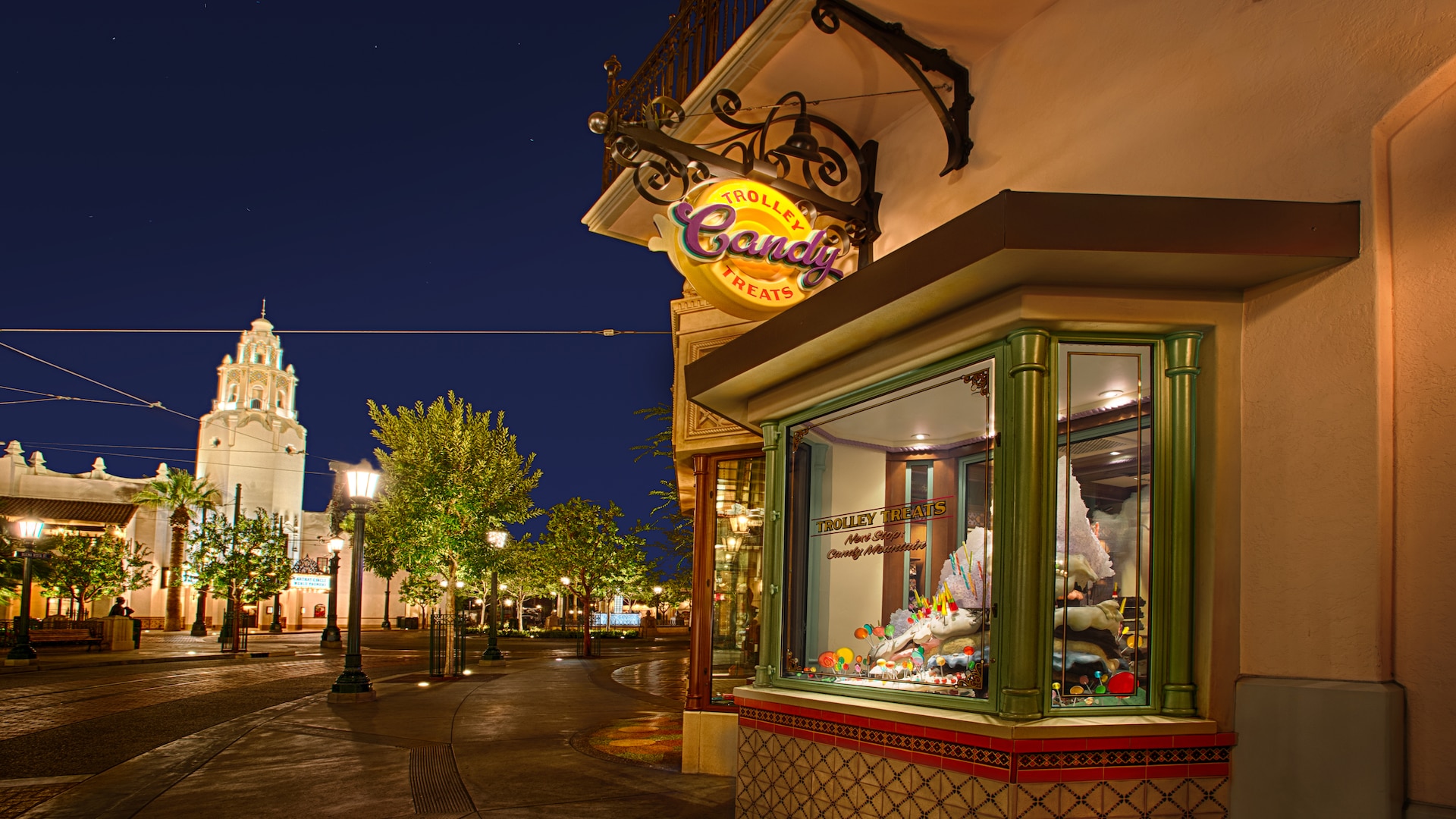 Buena Vista Street glowing at night as sweets are featured in the window display at Trolley Treats
