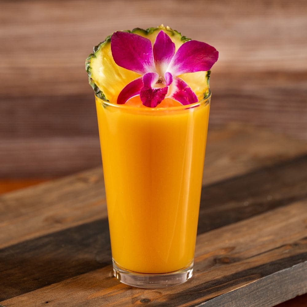 An orange smoothie garnished with a pineapple wedge and a blossom