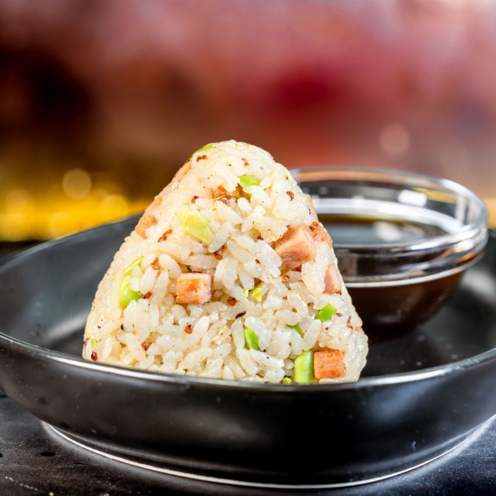 A plate with a Jonsior System Triangle from Oga’s Cantina with rice, ham, quinoa and edamame served with teriyaki sauce