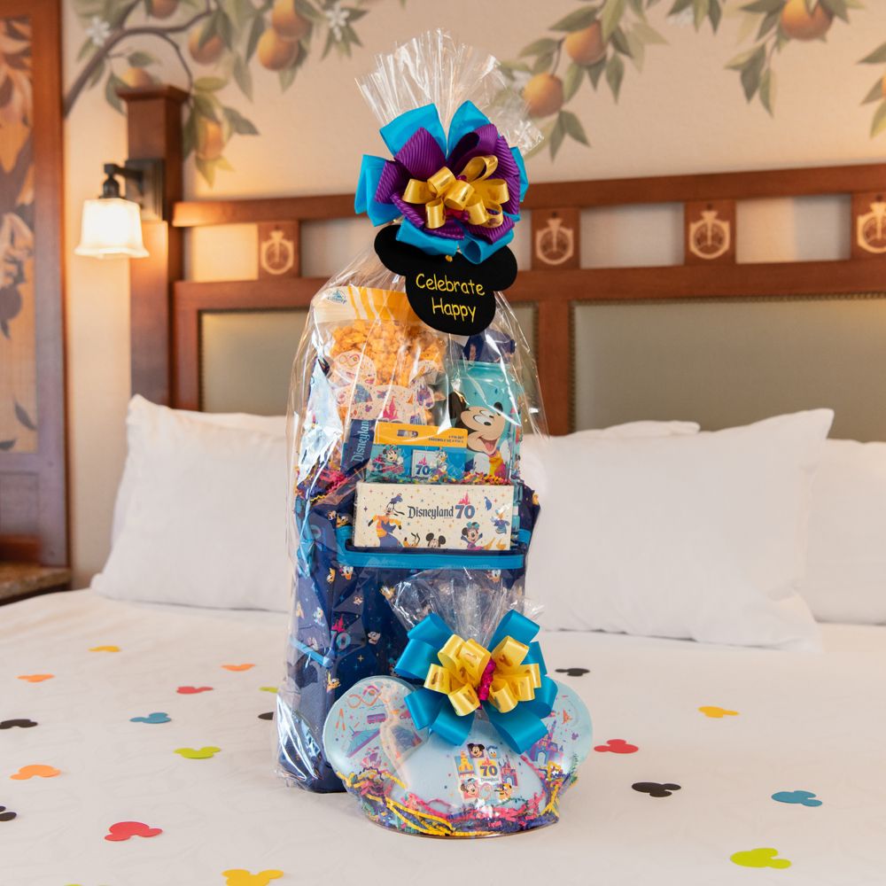 A Disneyland Resort 70th Celebration welcome basket with a bow and tag that says "Celebrate Happy" on a Disneyland Resort hotel bed