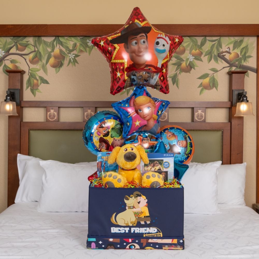 A Pixar welcome basket, plush Dug and balloons on a Disneyland Resort hotel bed