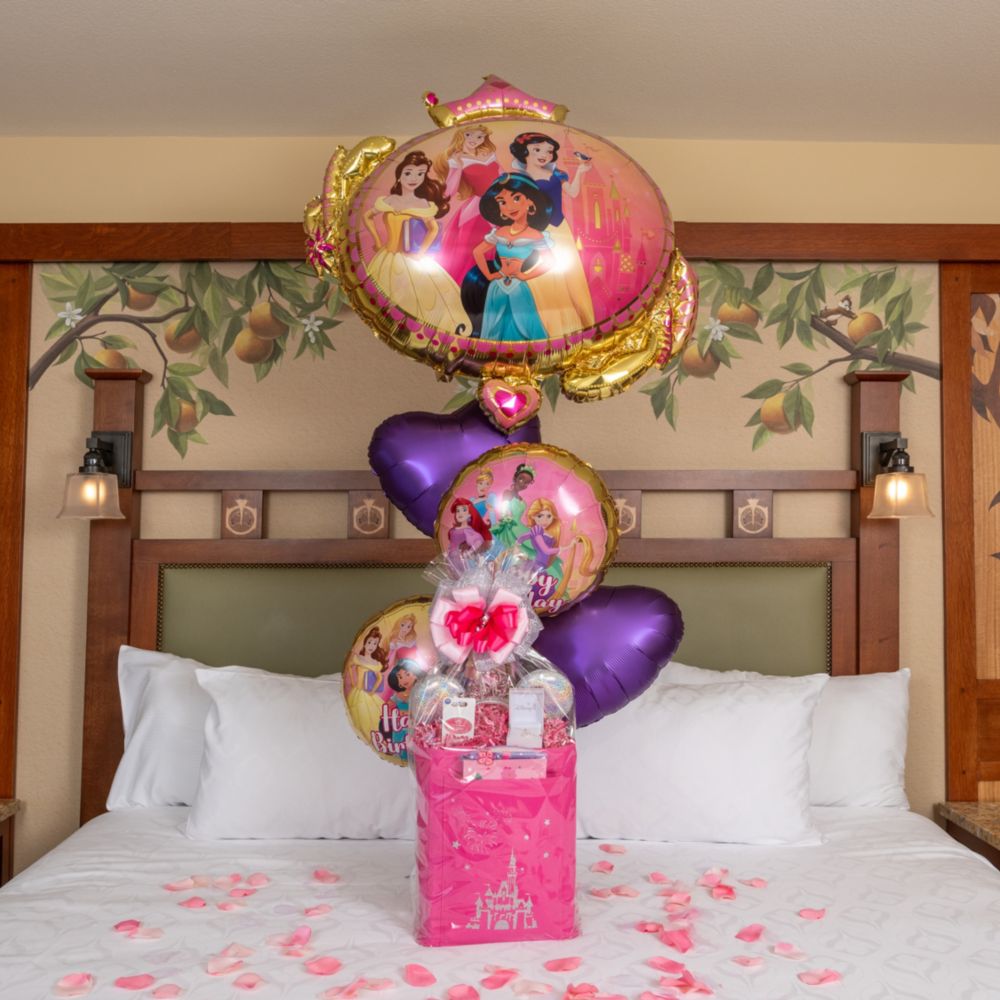 A Disney Princesses birthday welcome basket and balloons on a Disneyland Resort hotel bed