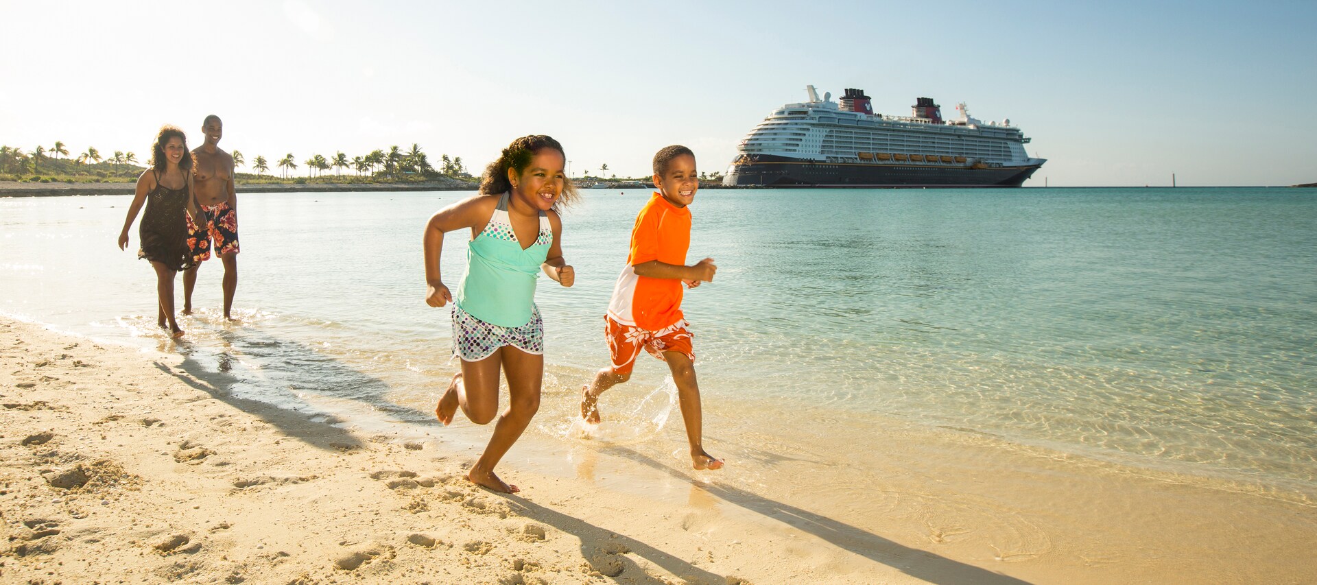 A Disney cruise ship docked next to a tropical island while 2 children run on the beach in front of their smiling parents
