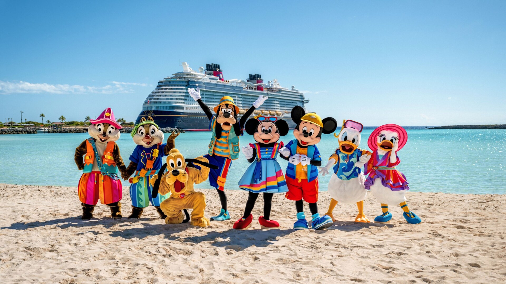 Mickey Mouse and friends stand wearing beach gear on the sands of Disney Castaway Cay as a Disney cruise ship sits docked behind them