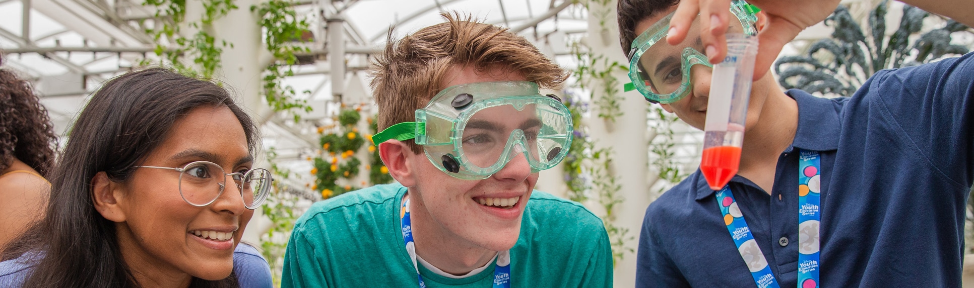 A Cast Member and 2 teenage boys in goggles staring in amazement at a test tube experiment