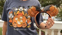 A Guest wearing a Halloween themed Disney Vacation Club shirt while holding a matching Minnie Mouse ear headband