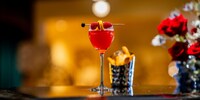 A glass of Membership Magic Martini with a raspberry and spiral orange zest garnish