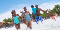 A family of 4 in bathing suits running through a water park 