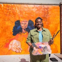Artista sosteniendo una paleta y pinceles frente a un mural en Disney Springs Art Walk