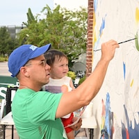 A man holds his child while painting a mural