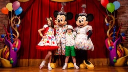 Dressed in party costumes, Mickey Mouse and Minnie Mouse pose with pair of young Guests on a stage