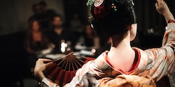 The back of a Japanese maiko in traditional dress, who is dancing with a fan in front of an audience The back of a Japanese maiko in traditional dress, who is dancing with a fan in front of an audience