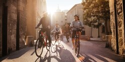 An Adventure Guide and several helmet-clad Adventurers ride bicycles on a street lined with stone buildings in Lyon, France 