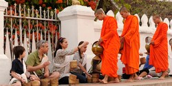 Monks collect daily alms from seated tourists