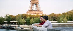 Two men stand with their arms resting on a cement railing overlooking the Seine River with the Eiffel Tower in the background