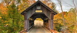 A head-on view of a wooden covered bridge with a sign that reads ‘No Trucks or Buses Allowed’ on a road surrounded by trees