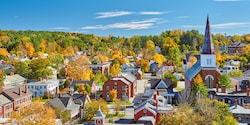The town of Montpelier, Vermont featuring a church with a large steeple and a large grove of trees The town of Montpelier, Vermont featuring a church with a large steeple and a large grove of trees