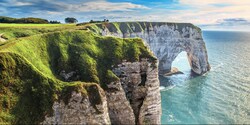 Grass covered cliffs with an arch-shaped structure rise high above the water Grass covered cliffs with an arch-shaped structure rise high above the water
