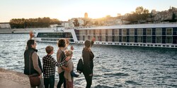 A group of people wave to a passing river boat ship from the shore A group of people wave to a passing river boat ship from the shore