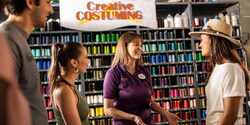 A Cast Member speaks to Guests in front of a wall filled with thread and a sign that reads, ‘Creative Costuming’ A Cast Member speaks to Guests in front of a wall filled with thread and a sign that reads, ‘Creative Costuming’