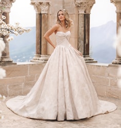 A woman in a strapless wedding dress standing on a stone balcony with arches and flowers