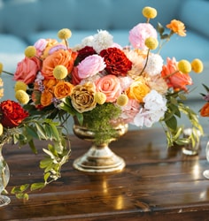 A large floral arrangement with roses and Billy Balls in a brass vase on a wood table